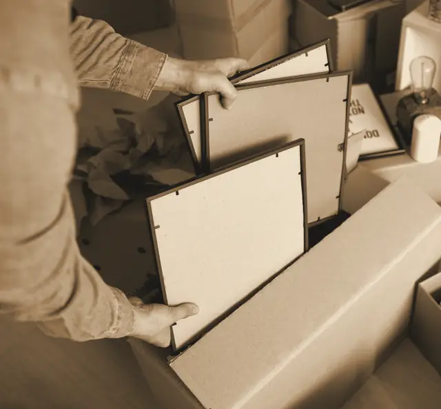 Manos guardando marcos de fotos en una caja de cartón durante el embalaje